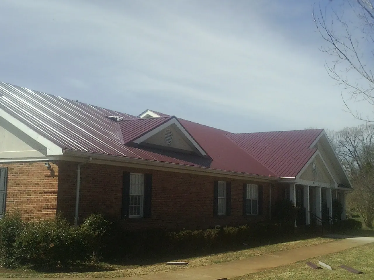 Red metal roof with gabled entries on a long brick building, from a Hail Damage Roof Repair job in Cedar