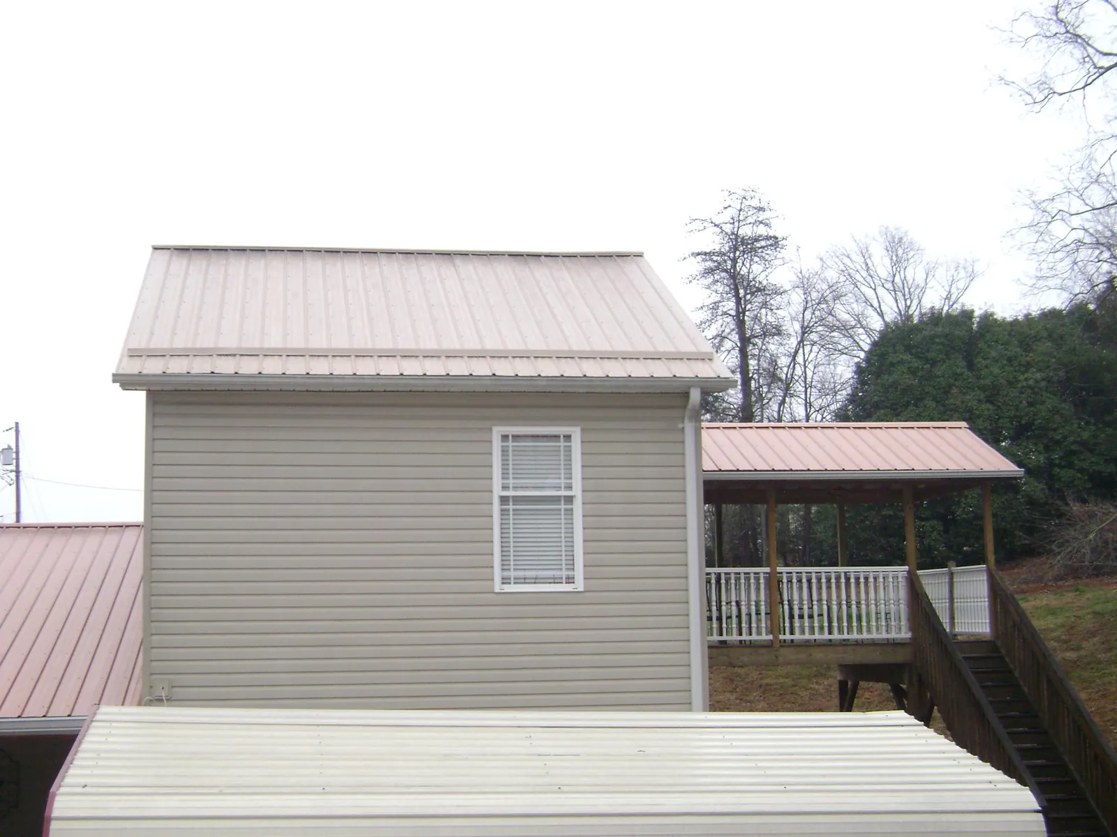 Tan metal roofs on a two story addition and attached porch, from a Roof Replacement job in Cedar